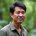 熱帯雨林を背景に微笑む40代の田中さん。